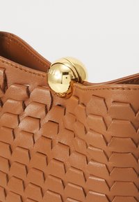 Sac en cuir tan avec un motif hexagonal texturé. Présente un fermoir rond en or avec "Furla" gravé. Doublure intérieure lisse.