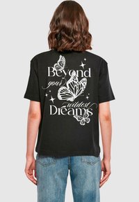 Svart t-skjorte med hvite sommerfugl-illustrasjoner og teksten "Beyond your wildest Dreams" på baksiden, korte ermer og avslappet passform.