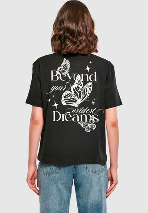 T-shirt noir avec des graphismes de papillon blancs et le texte "Au-delà de tes rêves les plus fous" au dos, à manches courtes et coupe décontractée.