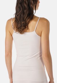 Jasnoróżowy top na ramiączkach z cienkimi paskami, wykonany z gładkiego, elastycznego materiału, o dopasowanym kroju, który podkreśla plecy i tułów.