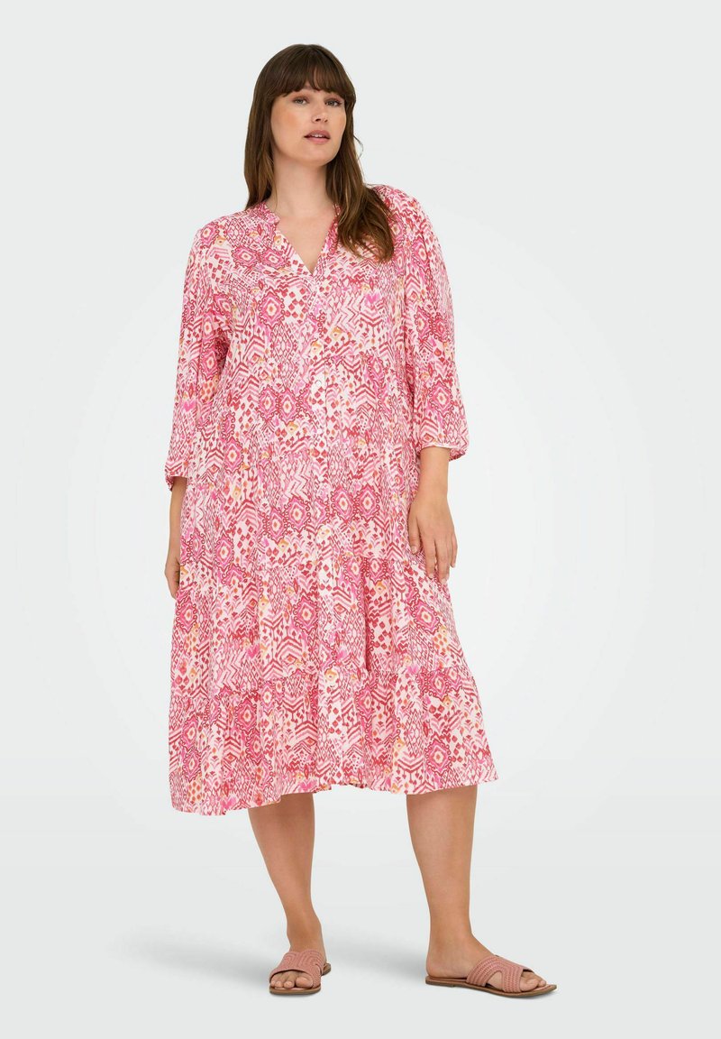 Abito rosa a fantasia con scollo a V, maniche a tre quarti, gonna a balze e tessuto leggero. Il design include motivi geometrici.