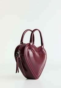 Borsa a forma di cuore in pelle bordeaux, con una finitura lucida, doppi manici e chiusura con zip accompagnata da una tracolla decorativa.