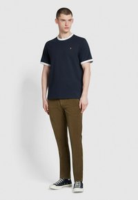 T-shirt navy con rifiniture bianche, maniche corte, presenta un piccolo logo. Abbinato a pantaloni verde oliva e sneaker nere.