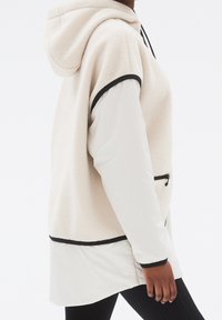 Överdimensionerad huvtröja, creamfärgad fleece med texturerad yta, med svarta detaljer, framficka med dragkedja och ett lagerdesign.