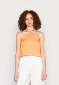 Top curto de cetim laranja com um design de pescoço halter e alças cruzadas. O tecido tem uma textura suave. Combinado com calças brancas de corte solto.