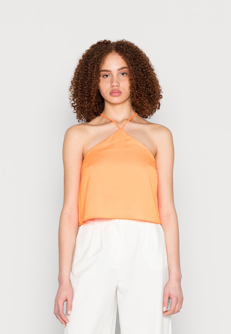 Top curto de cetim laranja com um design de pescoço halter e alças cruzadas. O tecido tem uma textura suave. Combinado com calças brancas de corte solto.