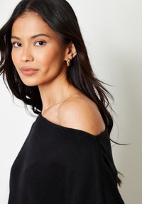 Zwarte off-the-shoulder trui met een zachte textuur. Heeft een ontspannen pasvorm en lange mouwen. Model draagt gouden creolen.