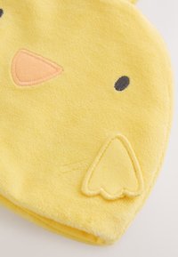 Sombrero de tela amarilla con forma de cara de pollito, con ojos negros bordados, pico naranja y detalle de ala sobre fondo blanco.