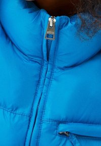 Modrá péřová bunda s vysokým límcem, s uzavřením na zip a stříbrnými detaily. Materiál má hladkou, lesklou texturu.