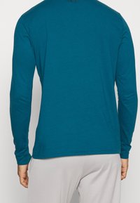 Pitkähihaisen turkoosin paidan, joka on valmistettu sileästä kankaasta, pyöreä kaula-aukko ja rento malli. Ei näkyviä kuvioita tai lisätietoja.