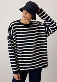 Sweter w niebiesko-białe paski wykonany z miękkiego materiału, o luźnym kroju i długich rękawach. Połączony z niebieską kapeluszem typu bucket.