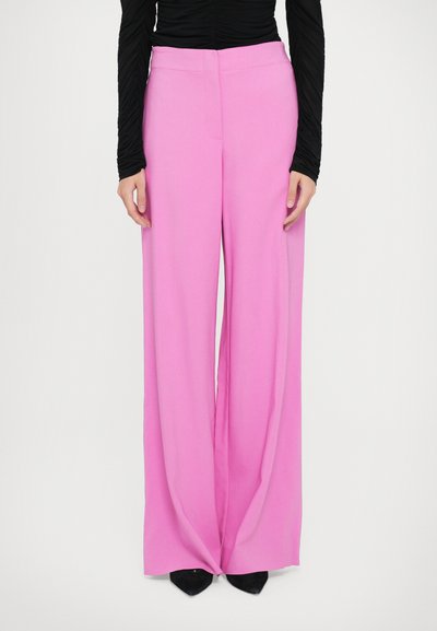 Pantalones de pierna ancha en rosa con una tela suave y ligera, talle alto y pliegues frontales, combinados con zapatos negros de punta.