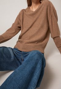 Bruine gebreide trui met een ontspannen pasvorm, verlaagde schouders en geribbelde zoom, gecombineerd met wijde blauwe denim jeans.