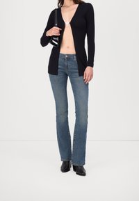 Cárdigan largo azul marino de manga larga con un escote en V profundo, abrochado en el pecho, combinado con unos vaqueros de campana de color azul claro y botines negros de tacón.