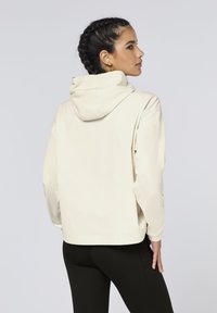 Cream-colored corduroy hoodie with a relaxed fit, visible seams, and a hood. Background is plain, emphasizing the garment's texture and design.