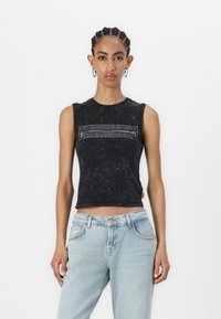 Svart ärmlös crop top med en texturerad yta och en framficka med dragkedja, kombinerad med ljusblå denimjeans.