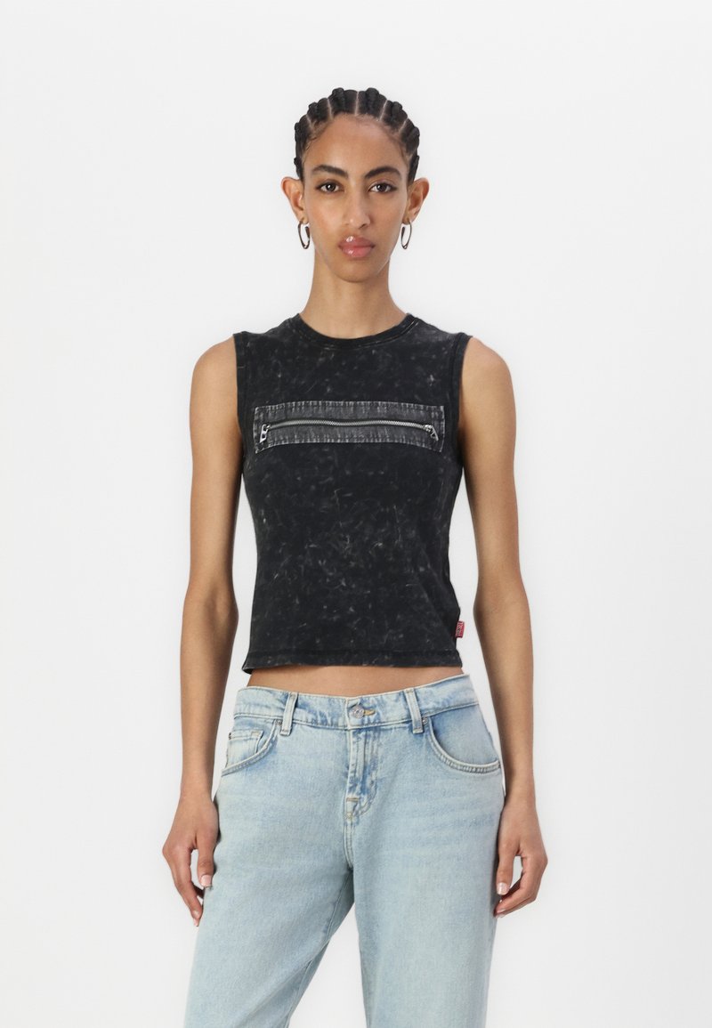 Svart ärmlös crop top med en texturerad yta och en framficka med dragkedja, kombinerad med ljusblå denimjeans.