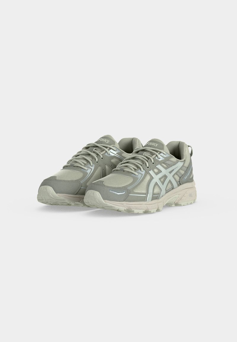 Par de zapatillas de running ASICS en gris claro y beige con malla y superposiciones sintéticas, colocadas una al lado de la otra sobre un fondo blanco.