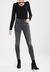 Černé dlouhé rukávy top s křížovým výstřihem, kombinovaný se šedými skinny džíny a černými koženými kotníkovými botami na podpatku. Hladký materiál s přiléhavým střihem.