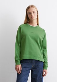 Grön sweatshirt med rund hals, raglanärmar och subtil text på framsidan. Matcher med mörkblå jeans som är tillverkade av mjukt tyg.