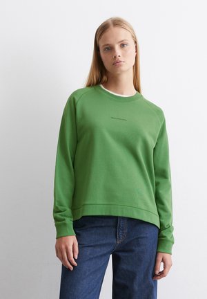 Felpa verde con scollatura rotonda, maniche raglan e testo discreto sul fronte. Abbinata a jeans blu scuro, realizzati in tessuto morbido.