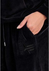 Schwarzer Samt-Hoodie mit einer Fronttasche, ausgestattet mit einem tonal gestickten Logo. Weiche Textur und Kordelzugdetails an der Kapuze.