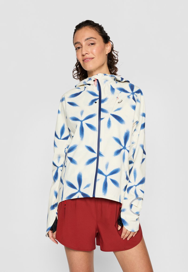 Leichte Zip-Jacke mit einem cremefarbenen Hintergrund und blauen Blumenmustern. Enthält eine Kapuze und Daumenlöcher an den Ärmelbündchen.