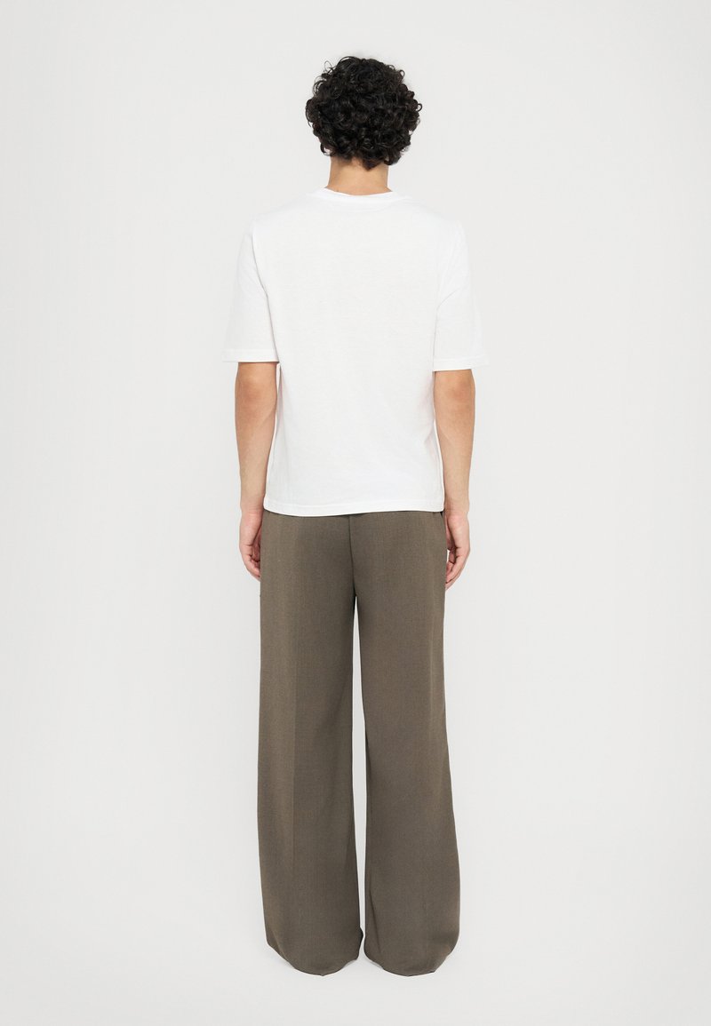 T-shirt blanche à manches courtes et pantalon vert olive ample, présentant une coupe droite et un tissu texturé, vu de dos.