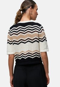 Hæklet sweater med et chevronmønster i sort, hvidt og varme jordfarver. Korte ærmer og tætsiddende taljedesign, der præsenterer struktureret strik.