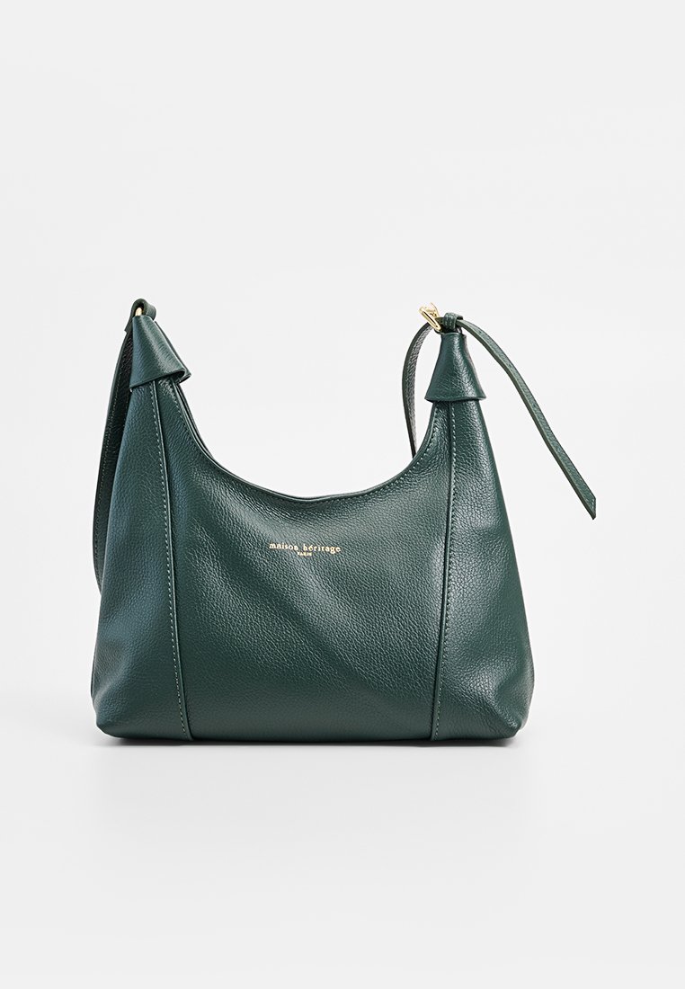 Bolso de cuero verde oscuro con una textura suave, que presenta un diseño asimétrico, acentos puntiagudos y un logo dorado en la parte frontal.
