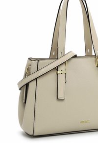 Ljus beige handväska i strukturerad läder med svarta detaljer, dubbla handtag och ett avtagbart band; guldlogotyp som framhävs tydligt.