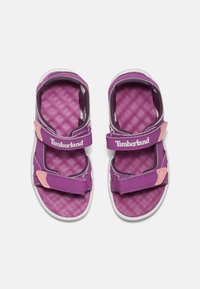 Violetit sandaalit, joissa on kaksinkertaiset tarrasiteet ja teksturoitu pohja. Ominaisuuksiin kuuluu valkoinen kumipohja ja Timberlandin brändäys valkoisena.