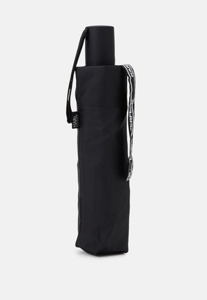 Black umbrella with a cylindrical handle, held in a matching fabric sleeve. Features a shoulder strap with logo detailing.