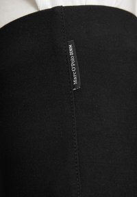 Must mustri, millel on sile tekstuur, lisaks on sellel õmmeldud sauma ja silt, millel on kirjas "Marc O'Polo DENIM" brändingu jaoks.