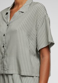 Short-sleeve, button-up blouse in light green with white vertical stripes, featuring a lapel collar and soft, smooth texture.