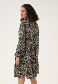Zwart-beige jurk met bloemenpatroon, ontspannen pasvorm, lange mouwen en een sleuteling in de rug. Lichtgewicht stof met een gelaagde zoom.