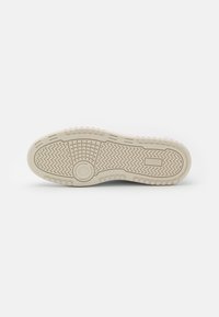 Semelle de chaussure en caoutchouc beige avec motifs en zigzag et en grille, affichée sur un fond blanc uni.