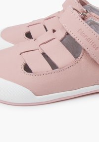 Zapatos de cuero sintético rosa con suelas de goma blanca, que presentan diseños recortados, correa ajustable y la marca "Blonditos" en el costado.