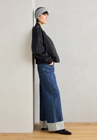 Black bomber jacket, wide blue denim jeans with frayed cuffs, and black pointed boots. Gray headband completes the outfit.