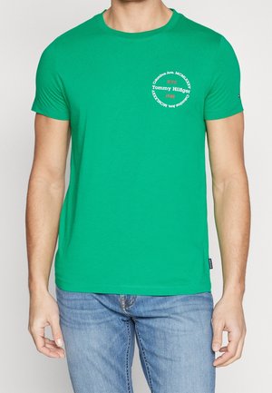 Zielona bawełniana koszulka z okrągłym dekoltem, krótkimi rękawami oraz okrągłym białym logo z napisem. Standardowy krój i gładka tekstura.