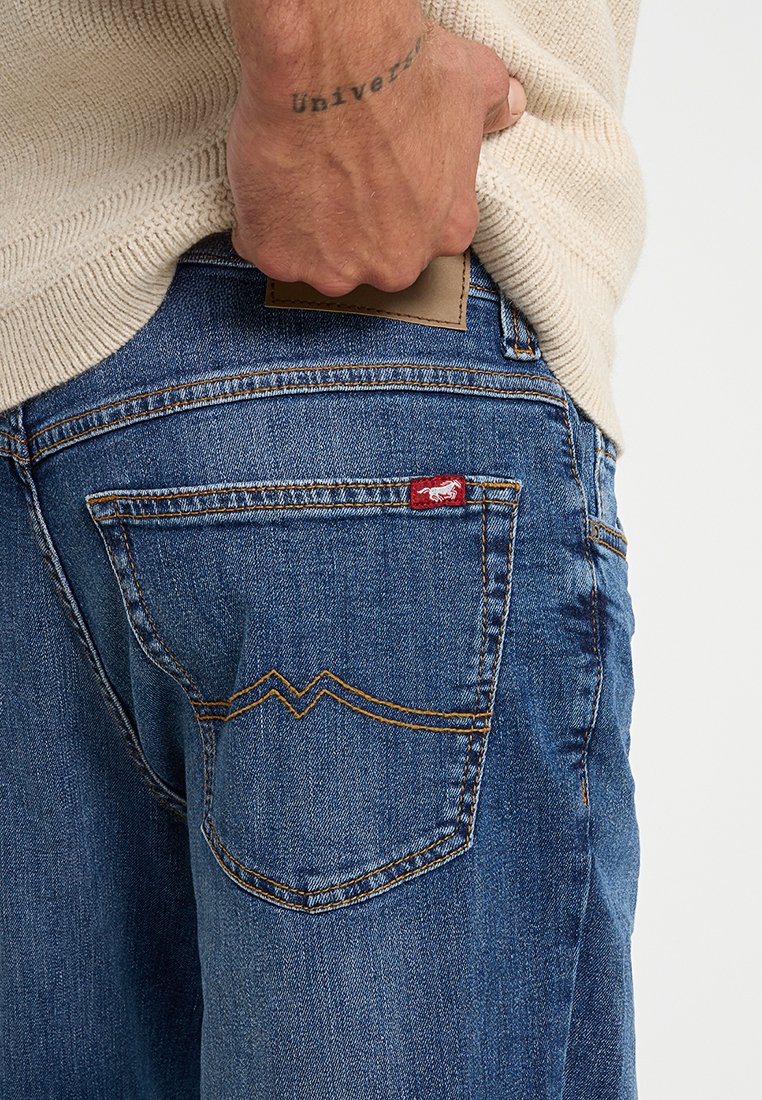 Niebieskie dżinsy o klasycznym kroju, z czerwoną metką brandingową i żółtym przeszyciem na tylnych kieszeniach, oraz skórzaną naszywką w pasie.