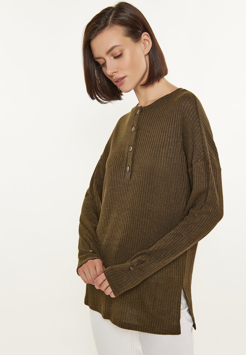 Olivgrünes, geripptes Langarmshirt mit rundem Halsausschnitt, drei Knopfverschluss und seitlichen Schlitzen am Saum. Weicher Stoff, entspannte Passform.