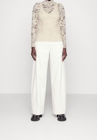 Lace long-sleeve top in beige over a cream-colored flowing pant; textured fabric and wide-leg design with black chunky shoes.