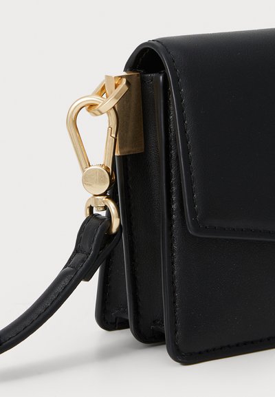 Sac à main en cuir noir avec un design structuré, doté de quincaillerie dorée, d'une bandoulière amovible et d'une texture lisse.