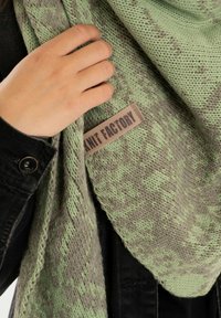 Zimowa chusta z zielono-szarym wzorem, wykonana z teksturowanego materiału dzianinowego, z metką z napisem "Knit Factory."