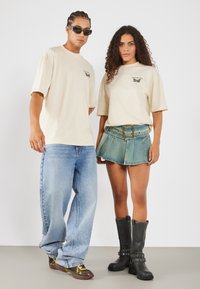 Beige oversized trička s černými potisky, světle modré široké džíny, denním mini sukně s přezkou a černé vysoké boty.