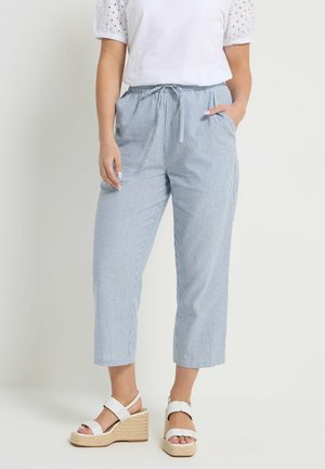 Femme portant un haut blanc à manches courtes en œillet, un pantalon court rayé bleu et blanc avec cordon de serrage, et des sandales à talons compensés blanches.