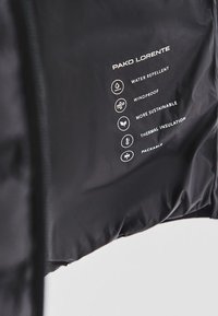 Czarna lekka kurtka o właściwościach wodoodpornych i wiatroszczelnych. Posiada izolację termiczną oraz możliwość spakowania, z nadrukowanymi ikonami pielęgnacyjnymi.