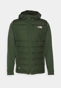 Veste matelassée vert foncé avec capuche, fermeture éclair complète à l'avant, poche poitrine, poches latérales et logo The North Face sur la poitrine.