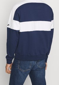 Mörkblå sweatshirt med vita horisontella ränder, ribbade muddar och nederkant, tillverkad av mjukt material. Har en liten svart logotyp på vänster ärm.